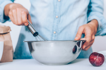 Close-up young woman's hands holding whisk and metal bowl