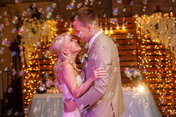 First wedding dance of stunning bride and attractive groom, cheerfully smiling, bubbles. Love. Marriage. Indoors.