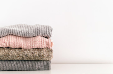 Stack of neatly folded knitwear. Minimal lifestyle, capsule wardrobe. Detail of cozy winter interior