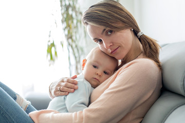 Young mother, holding her sick toddler boy, hugging him at home © Tomsickova
