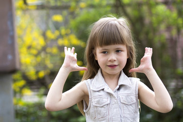 Portrait of a pretty little long-haired blond preschool girl in sleeveless white dress smiling...