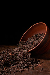 Dry tea leaves in clay bowl on black background. selective focus