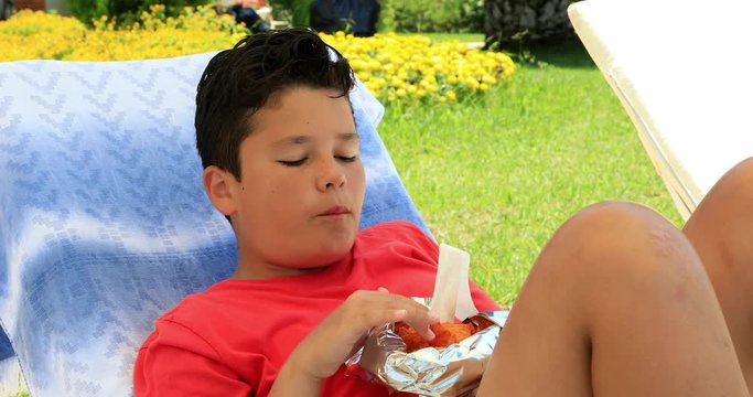 Portrait of a cute preteen schoolboy laying on a sunbed and eating potato chips