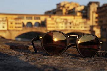 The setting sun reflecting in a pair of sunglasses with Ponte Vecchio in the background