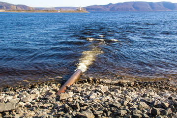 Dirty water flows out of a large metal rusty pipe under pressure into the river.