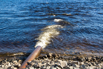 Dirty water flows out of a large metal rusty pipe under pressure into the river.