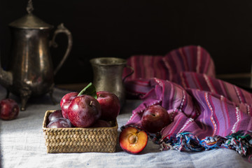 Fresh plum. Autumn harvest. Red plums. Yellow plum. Fresh plums on a wooden surface. Fresh plums on wooden table background with napkin and vintage kettle and glass. Bronze ware.