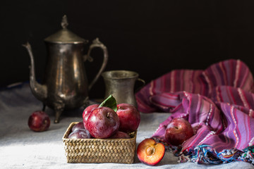 Fresh plum. Autumn harvest. Red plums. Yellow plum. Fresh plums on a wooden surface. Fresh plums on wooden table background with napkin and vintage kettle and glass. Bronze ware.