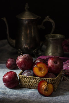 Fresh plum. Autumn harvest. Red plums. Yellow plum. Fresh plums on a wooden surface. Fresh plums on wooden table background with napkin and vintage kettle and glass. Bronze ware.