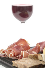 Selection of cold cuts and cheese on a platter with a glass of red wine. White background
