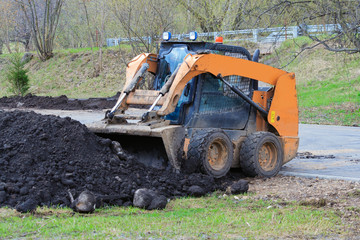 Works on the improvement of the park area. Skid  steer loader rakes black soil into bucket