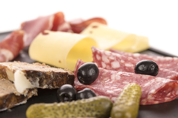 Gherkins, olives and cold cuts and cheese on a platter. White background.