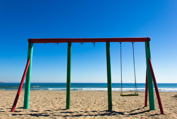Single swing and two more missing on sunny winter day in La Serena beach, Chile. Kids playground by the sea