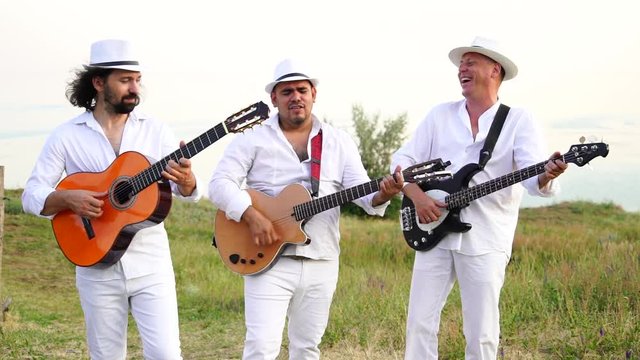 Musicians in white clothes and white hats play the guitars. Cuban musicians on the coast. Slow motion.