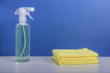 Cleaning or housekeeping concept. A bottle of detergent and microfiber cloths on blue background.