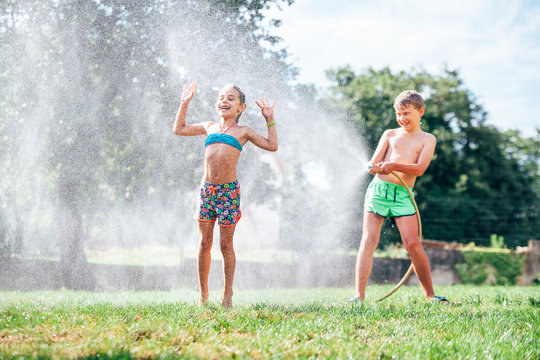 Two child, brother and sister, play with watering hose in hot summer afternoon