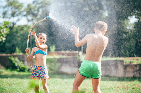 Two childs, brother and sister, have fun, when play with watering hose in summer garden