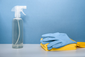 Cleaning or housekeeping concept. A bottle of detergent, protective gloves and microfiber cloths on blue background.
