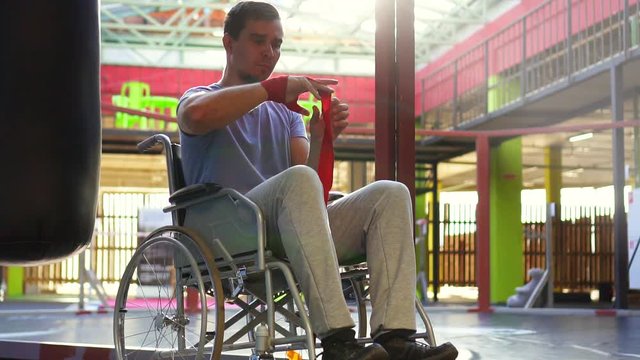 Man with a disability in a wheelchair wound boxing tapes on his hands.Slow mo