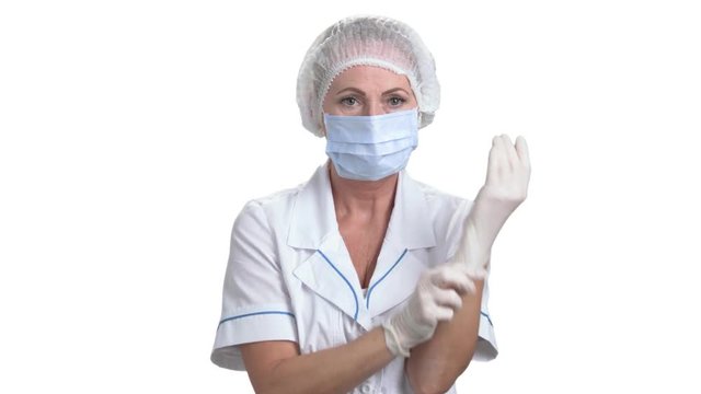 Female surgeon putting on a glove. Female medicine doctor in protective mask and cap putting on white protective glove, white isolated background.