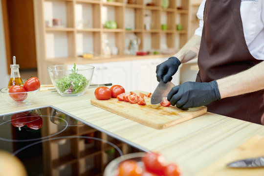 Closeup of unrecognizable male chef cutting vegetables standing at wooden table in restaurant kitchen, copy space