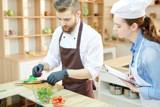 Portrait of two professional chefs working in restaurant kitchen together cooking and seasoning salad standing at wooden table
