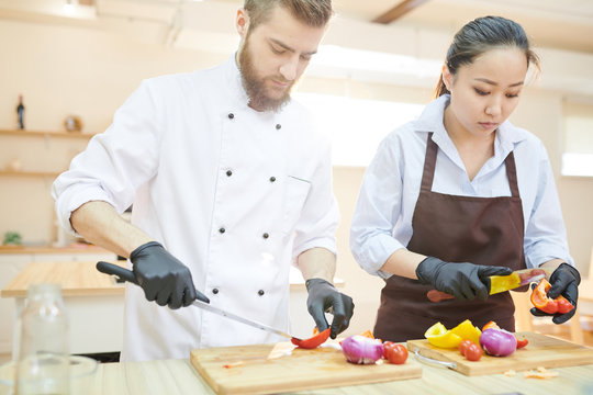 Waist up  portrait of two professional cooks working in restaurant kitchen cutting vegetables standing at wooden table, copy space