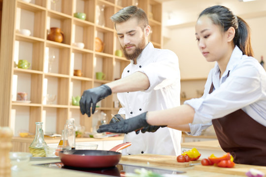 Portrait of two professional cooks working in restaurant kitchen seasoning dishes standing  at wooden table, copy space