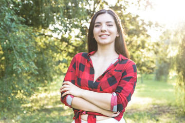 Smiling beautiful brunette girl in a red, plaid shirt, with arms crossed