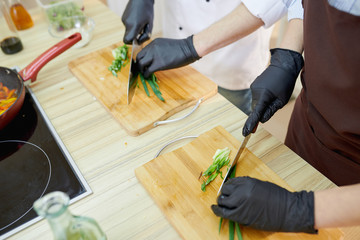 High angle closeup of unrecognizable chefs cutting vegetables standing at wooden table in...