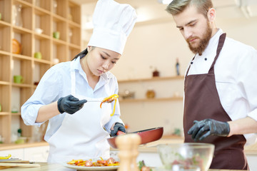 Waist up  portrait of focused female Asian chef cooking delicious dishes while working in modern restaurant kitchen with su-chef, copy space
