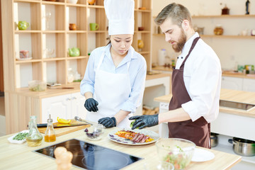 Fototapeta na wymiar Waist up portrait of two professional chefs cooking delicious dishes in modern kitchen standing at wooden table , copy space