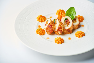 Poultry rolls with carrot puree, orange on a white plate