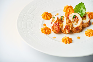 Poultry rolls with carrot puree, orange on a white plate