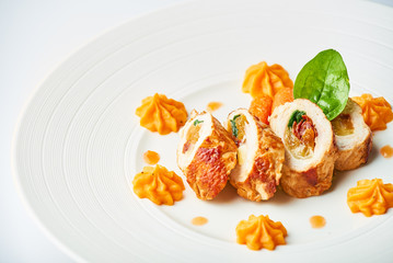 Poultry rolls with carrot puree, orange on a white plate