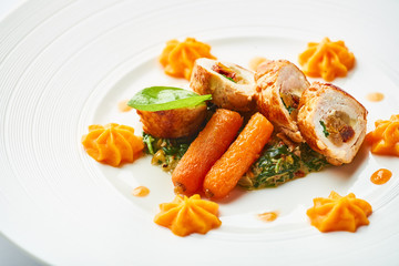 Poultry rolls with carrot puree, orange on a white plate