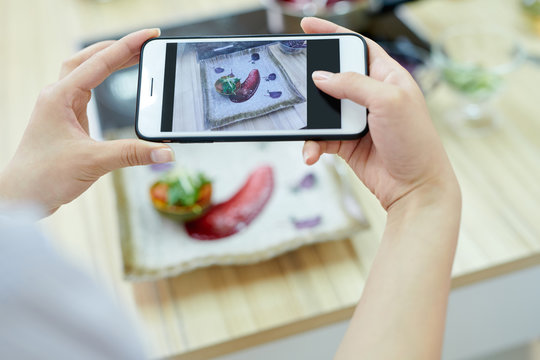 Close up of unrecognizable woman holding smartphoneand taking picture of delicious dish in restaurant, focus on screen