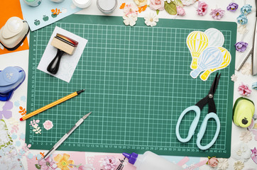 Multi-colored paper, scrapbooking tools and materials on green mat for cutting, top view, no hands