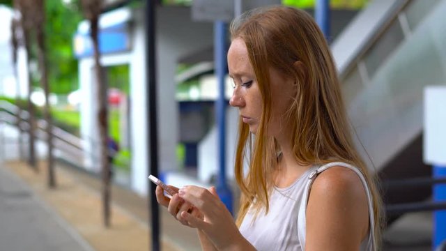 Young woman on a street lost in big city, trying to search through the map on her phone and book a taxi