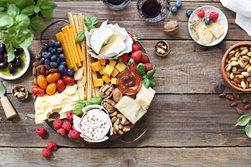 Cheese platter with fresh berries and nuts on a rustic wooden table. Overhead view.