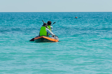 Fototapeta na wymiar Two male tourists wearing green life jackets, helping Paddle with rubber boats, are in the clear, clean sea water at Koh Samet, a popular tourist destination in Thailand.