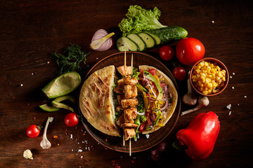 Exotic still slife with pita, fresh vegetables and kebab over wooden background, selective focus.