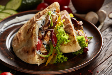 Pita stuffed with chicken, beans and letucce on clay plate over wooden background, side view,...