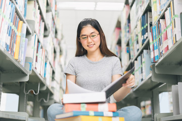 Asian Woman reading and sitting near a bookshelf in the library..