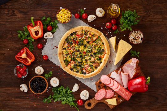 Pizza still life. Freshly baked pizza and its components arranged on wooden background.