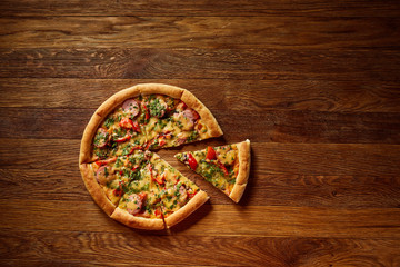 Freshly baked pizza divided into slices on rustic wooden background, top view, close-up, selective focus.