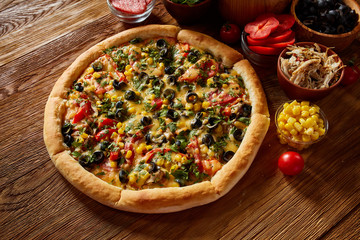 Pizza still life. Freshly baked pizza and its components arranged on wooden background.