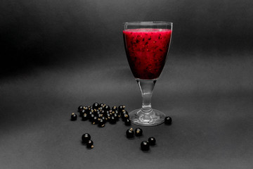 Glass of black currant red color cocktail in grey background with berries on it