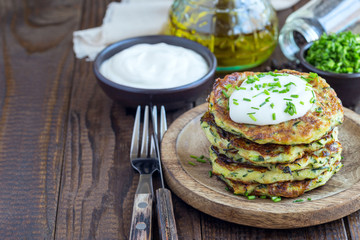 Vegetarian zucchini fritters or pancakes, served with greek yogurt and green onion on wooden background, horizontal, copy space
