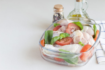 Raw uncooked chicken legs, drumsticks with tomatoes and basil in glass backing dish, meat with ingredients for cooking, horizontal, copy space